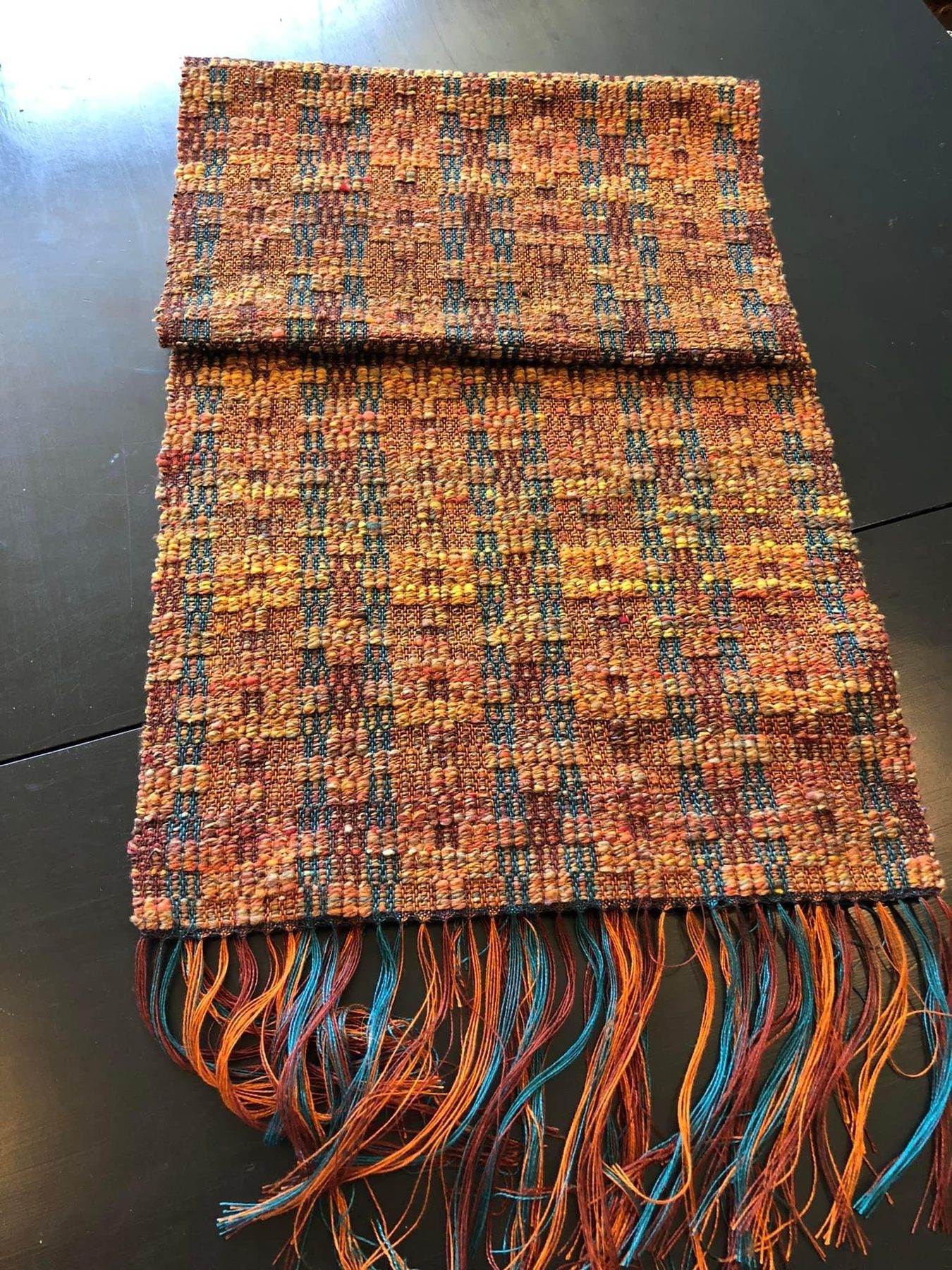Rust, orange, and teal handwoven fringed scarf folded neatly